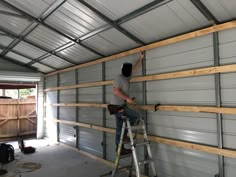 a man standing on a ladder in front of a garage door with wood planks