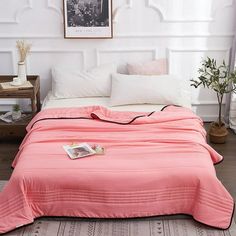 a bed with a pink comforter on top of it next to a white wall