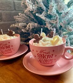 two pink cups filled with food on top of a wooden table next to a christmas tree