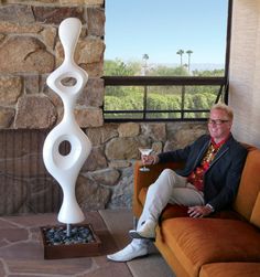 a man sitting on top of a couch next to a tall white vase in front of a window