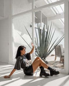 a woman is sitting on the floor in front of a window and looking at a cactus