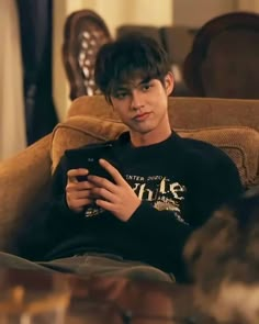 a young man sitting on top of a brown chair holding a cell phone in his hand