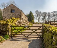 a stone building with a wooden gate and moss growing on the fence surrounding it is surrounded by trees