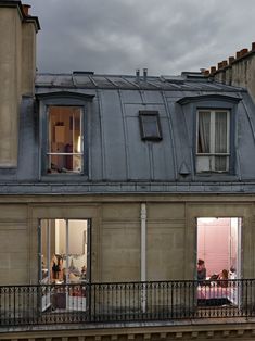 two people are sitting on the balcony of an apartment building, looking out onto the street