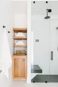 a bathroom with white tile and wooden shelving next to a walk - in shower