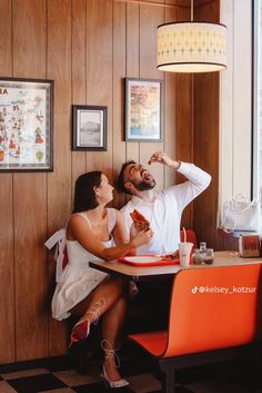 a man and woman sitting at a table in a restaurant, one is eating pizza