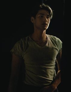 a young man standing in the dark with his hand on his hip and looking off into the distance