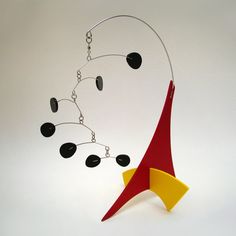 a red and yellow sculpture with black stones hanging from it's sides on a white background