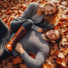 two beautiful women laying on the ground with autumn leaves in front of them and smiling at the camera