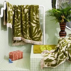 a bathroom with green tile and towels hanging on the shower curtain, potted plant and towel rack