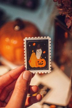 someone is holding up a small stamp with a cat on it and pumpkins in the background