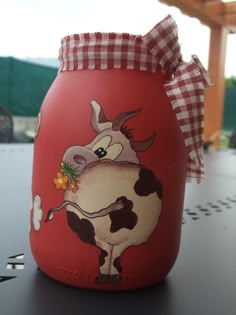 a red jar with a cow painted on it's side sitting on a table