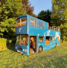 a blue double decker bus parked on top of a grass covered field next to trees