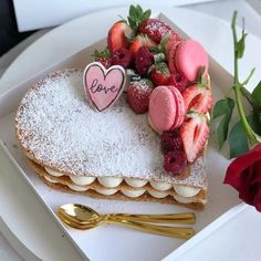 a heart shaped cake with strawberries and powdered sugar on top, sitting on a plate next to a rose