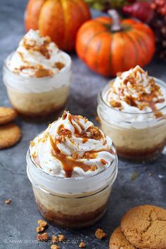 three desserts in small glass jars with cookies and pumpkins behind them on a table