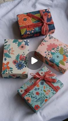 four wrapped presents sitting on top of a white tablecloth covered in flowers and ribbons