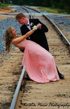 a man in a tuxedo and a woman in a pink dress on train tracks