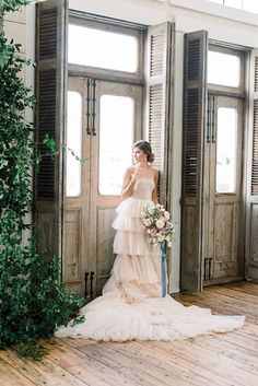 a woman standing in front of two doors wearing a wedding dress and holding a bouquet