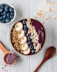 a bowl filled with blueberries, bananas and granola next to a wooden spoon