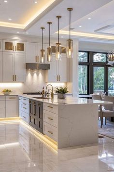 a large kitchen with white cabinets and marble counter tops, along with lights hanging from the ceiling