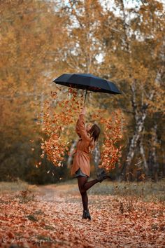 a woman holding an umbrella over her head while standing in the middle of autumn leaves