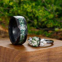 a couple of rings sitting on top of a wooden table next to some bushes and trees