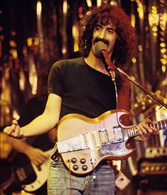 a man with long hair playing an electric guitar and singing into a microphone on stage