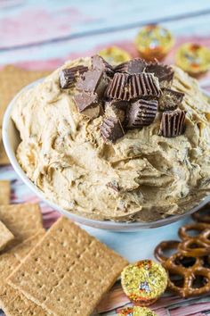 a bowl filled with peanut butter dip surrounded by pretzels and crackers