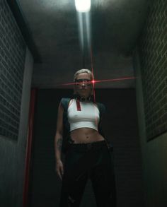 a woman in white shirt and black pants standing next to brick wall with red light