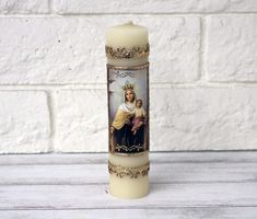 a lit candle with an image of the virgin mary and jesus on it sitting in front of a white brick wall