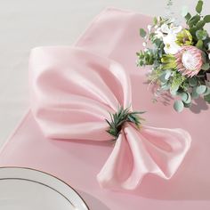 a pink napkin with a flower on it next to a white plate and silverware