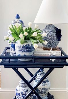 blue and white vases with flowers on a tray next to a lamp in a living room