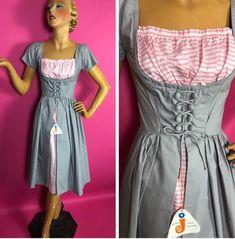 This is a lovely cotton dress by Wards Junior Fashions.  It has never been worn and still has its tag attached.  The dress itself has a union made label.  It is made of two fabrics: a warm concrete grey solid and a pink and white stripe.  It is made in the dirndl dress style. It has short sleeves.  The bodice is cut low with a fitted midriff to the waist.  The midriff has decorative lacing.  There is an inset of gathered pink and white stripe fabric in the very low neckline, like a modesty panel 1950s Cotton Vintage Dress For Vintage Fashion Events, 1950s Cotton Vintage Dress, 1950s Style Cotton Vintage Dress, Retro Vintage Cotton Dress With Square Neck, Dirndl Style, Bavarian Dress, Oktoberfest Dress, Modesty Panel, Uniform Dress