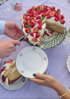 two people are cutting into a cake with strawberries on top