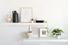 a white shelf with some vases and pictures on it next to a potted plant