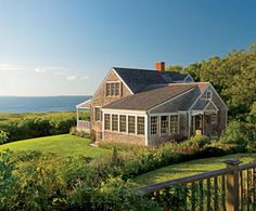 the house is surrounded by lush green grass and trees, with an ocean view in the background