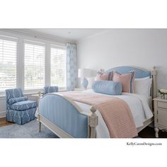 a bedroom with blue and pink bedding, two chairs and windows in the background