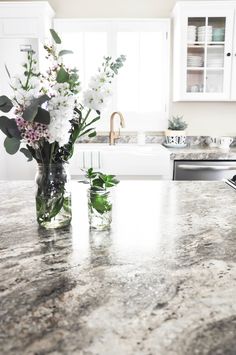 two vases filled with flowers on top of a kitchen counter