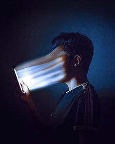 a person holding a book in their hands with the light coming from it's face