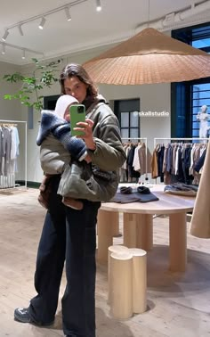 a woman holding a baby in her arms while looking at a cell phone with clothes on display