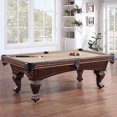 a pool table in the middle of a living room with wood flooring and white walls