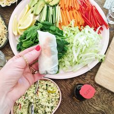 a person holding a vegetable roll over a plate of vegetables and other foods on a table