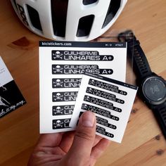 a person holding up some stickers on top of a wooden table next to a helmet