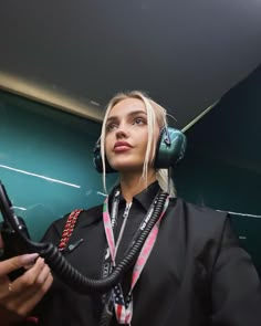 a woman wearing headphones and holding a microphone in front of her face while standing next to a green wall