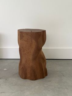 a wooden stool sitting on top of a cement floor next to a white wall and potted plant