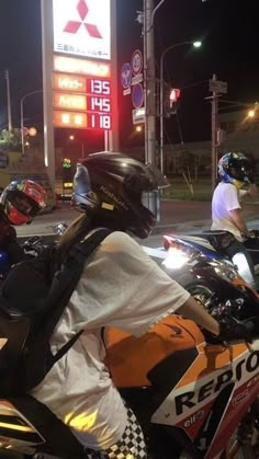 two motorcyclists are stopped at a gas station