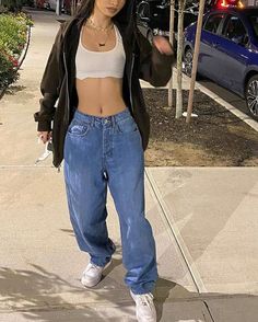 a woman in jeans and a crop top is walking down the sidewalk with an umbrella