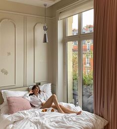 a woman laying in bed next to a window