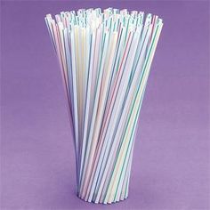 multicolored paper straws are in a tall cup on a purple tablecloth