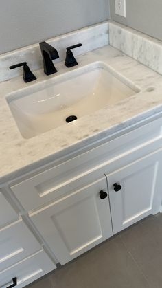 a white bathroom vanity with marble top and two black faucets on the sink